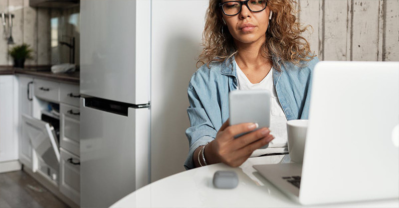 woman on her phone with coffee at kitchen table